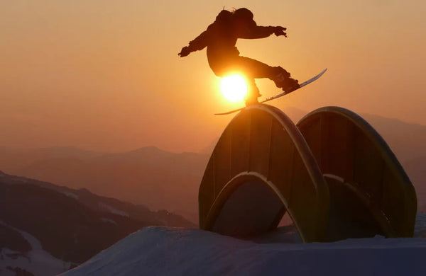 Snowboarder slinding over a rainbow rail in the susnset