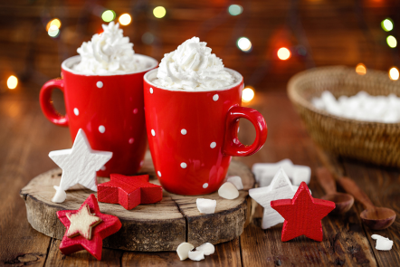 Two cups of coffee in festive red mugs topped with whipped topping and shredded coconut.