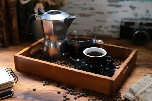 moka pot and mug sitting in a wooden tray surrounded by coffee beans