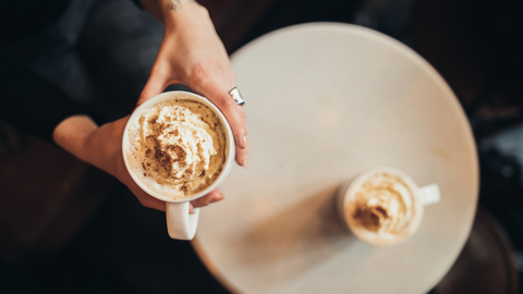 woman's hands holding a coffee topped with whipped cream and sprinkled with pumpkin spice