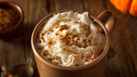 close up image of a coffee topped with whipped cream and sprinkled with pumpkin spice