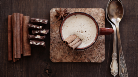 Latte with cinnamon sticks and pieces of chocolate
