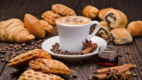 cup of cinnamon topped latte surrounded by pastries