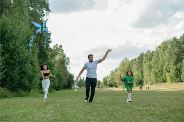 Young Asian family playing with a kite together and being active in a park.