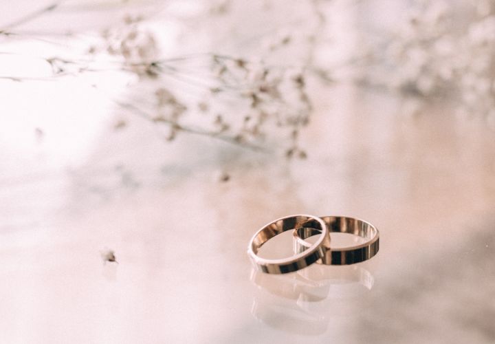 Two silver rings on a glass table with flowers on the background.