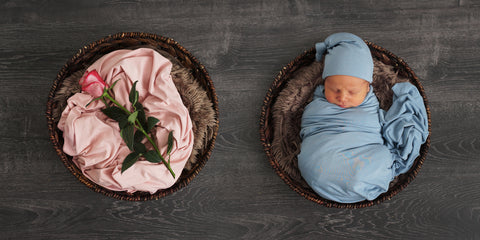 Newborn photo showing one baby in a blue swaddle in a basket, and a pink rose on top of a pink swaddle in a separate basket.