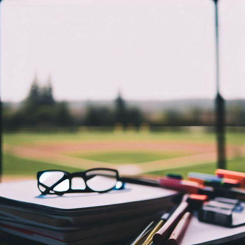 School supplies in the foreground with a baseball diamond in the backdrop.