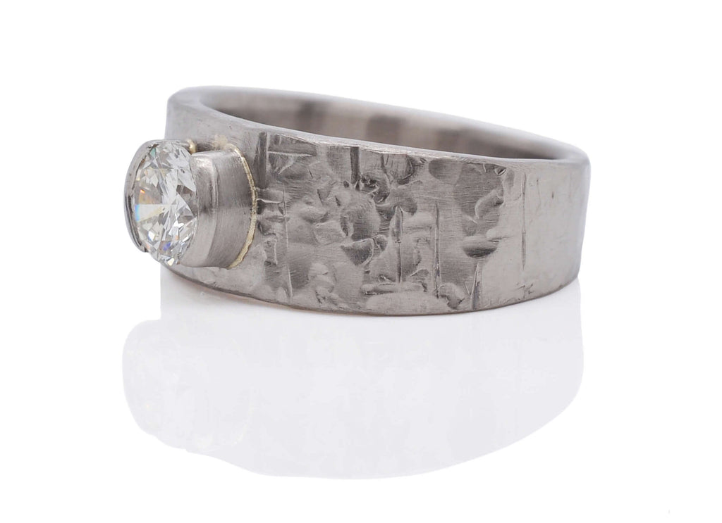 wide hammered white metal wedding ring with a raised white diamond in a half bezel and a crushed hammered texture.