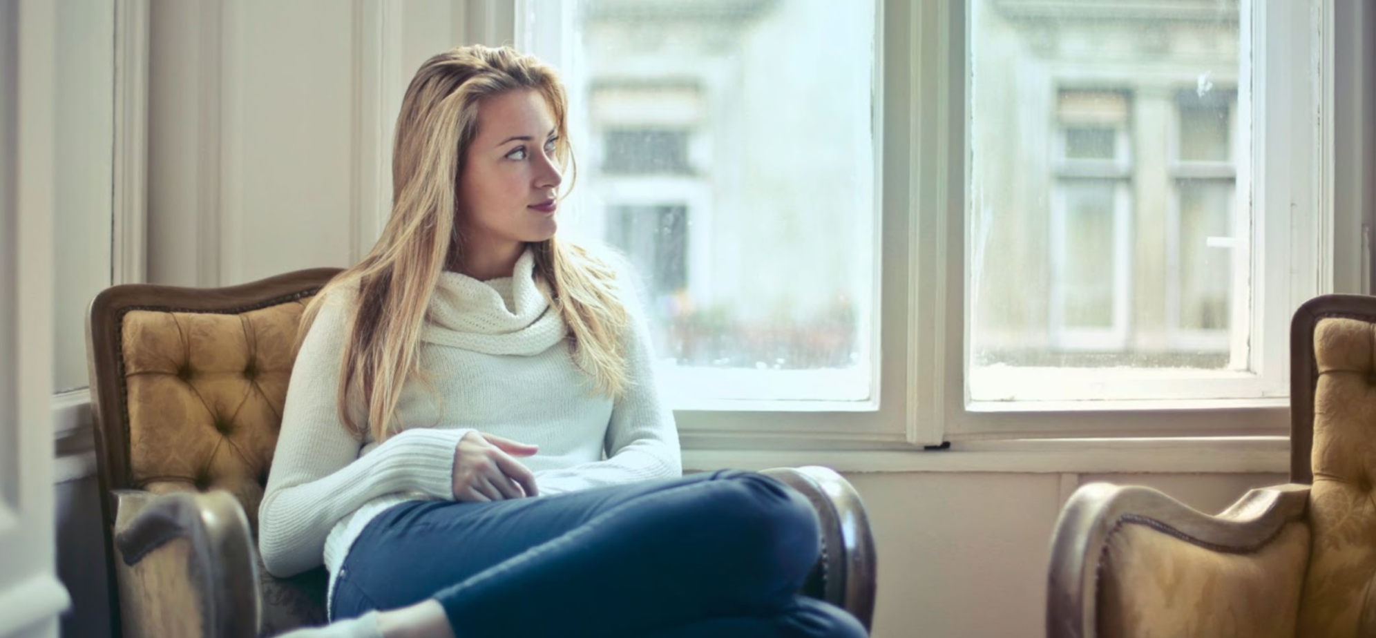 Woman in a white jumper, curled up and resting on a chair