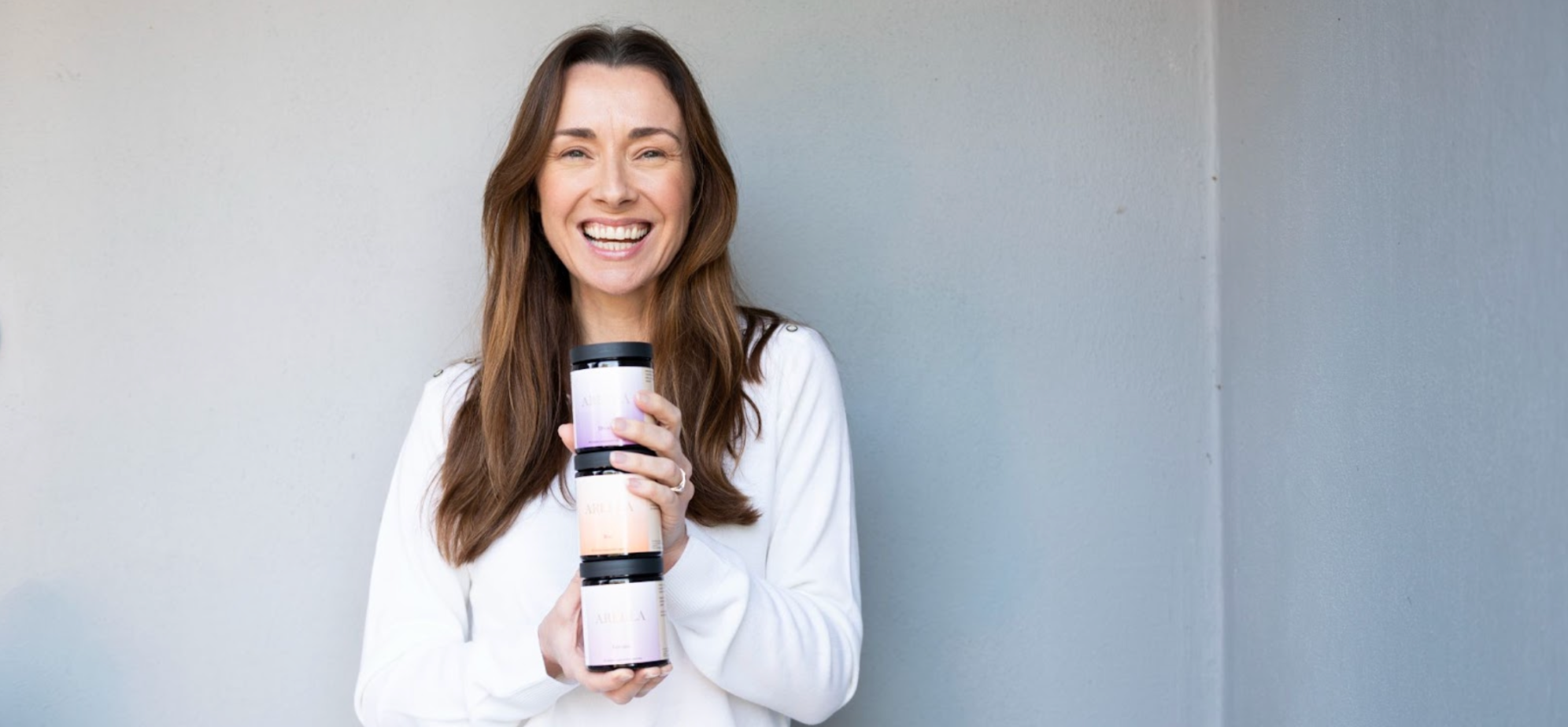 Woman with long brown hair holding Arella Beauty supplements