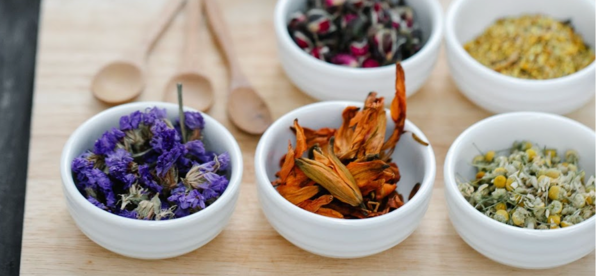 Bowls of dried herbs and flowers on a wooden chopping board