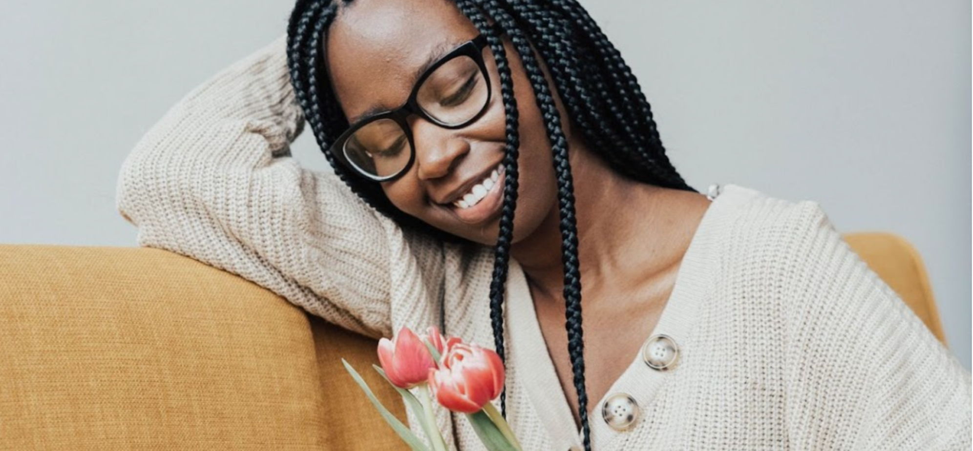 Woman wearing glasses with closed eyes, smiling and holding tulips