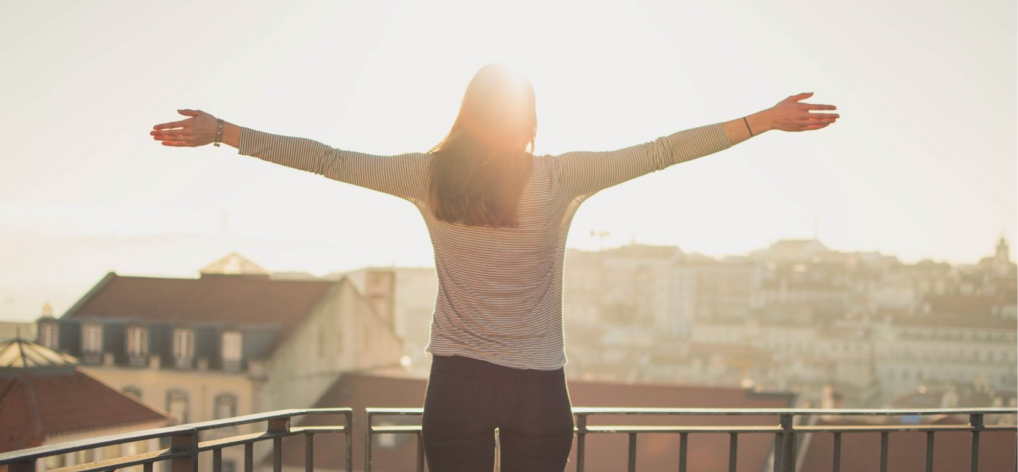 Woman with her arms out, standing in front of the sun