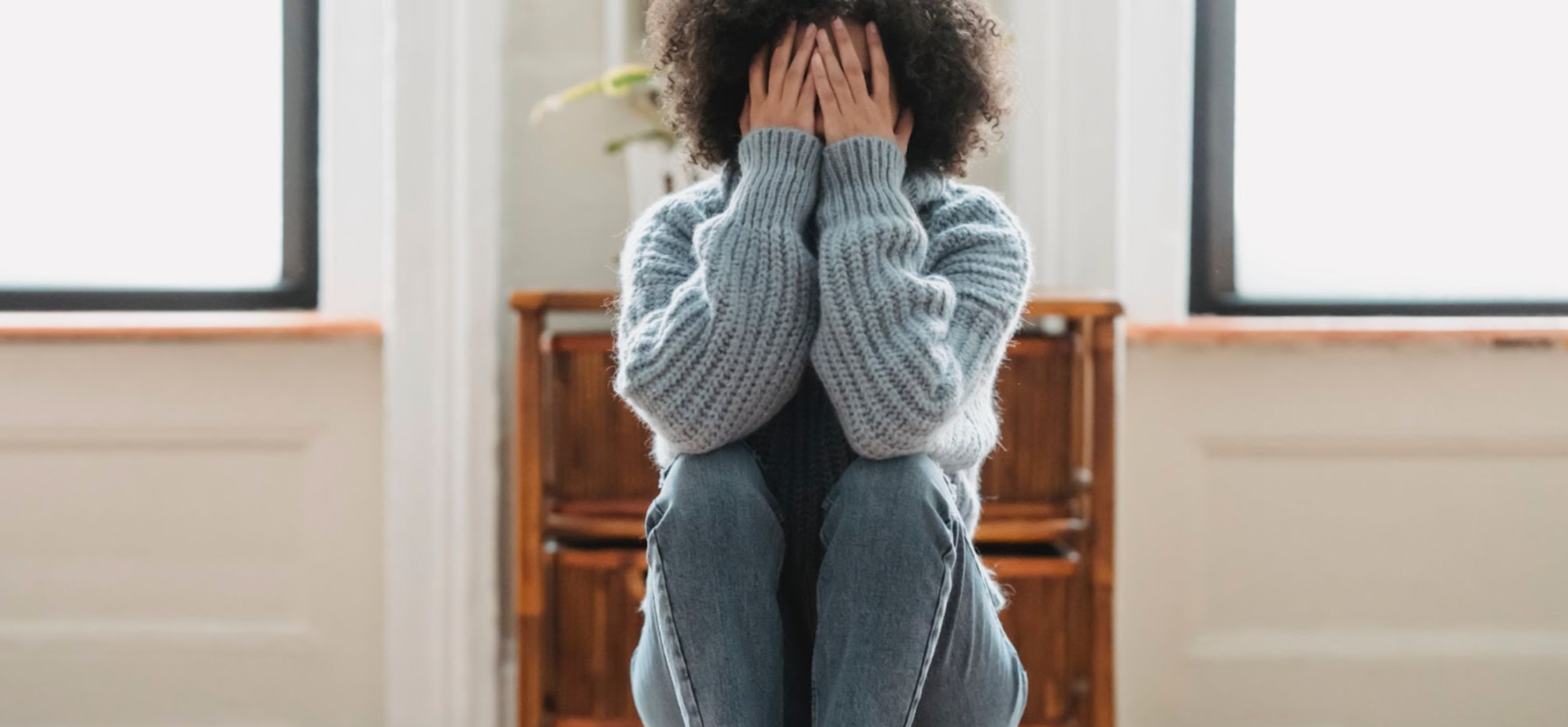 Sad woman sitting down, wearing a blue jumper and jeans