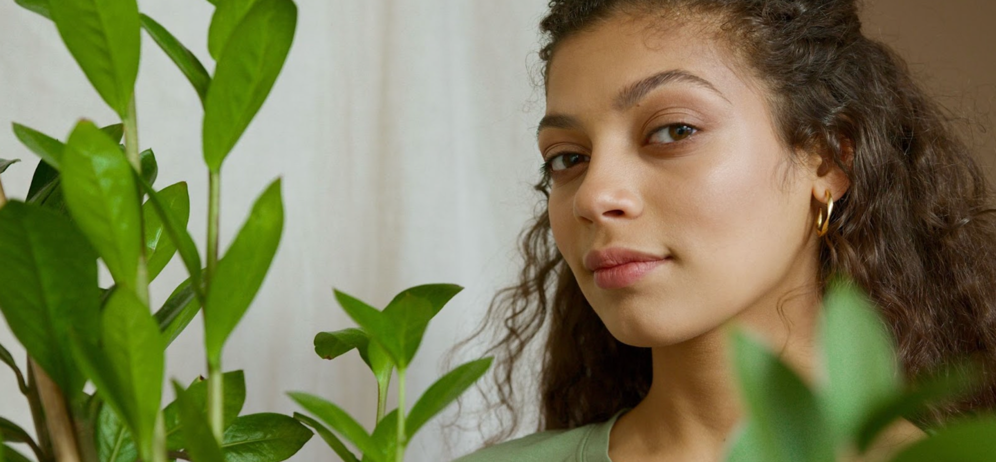 Woman with dark, curly hair in a green t-shirt next to a plant