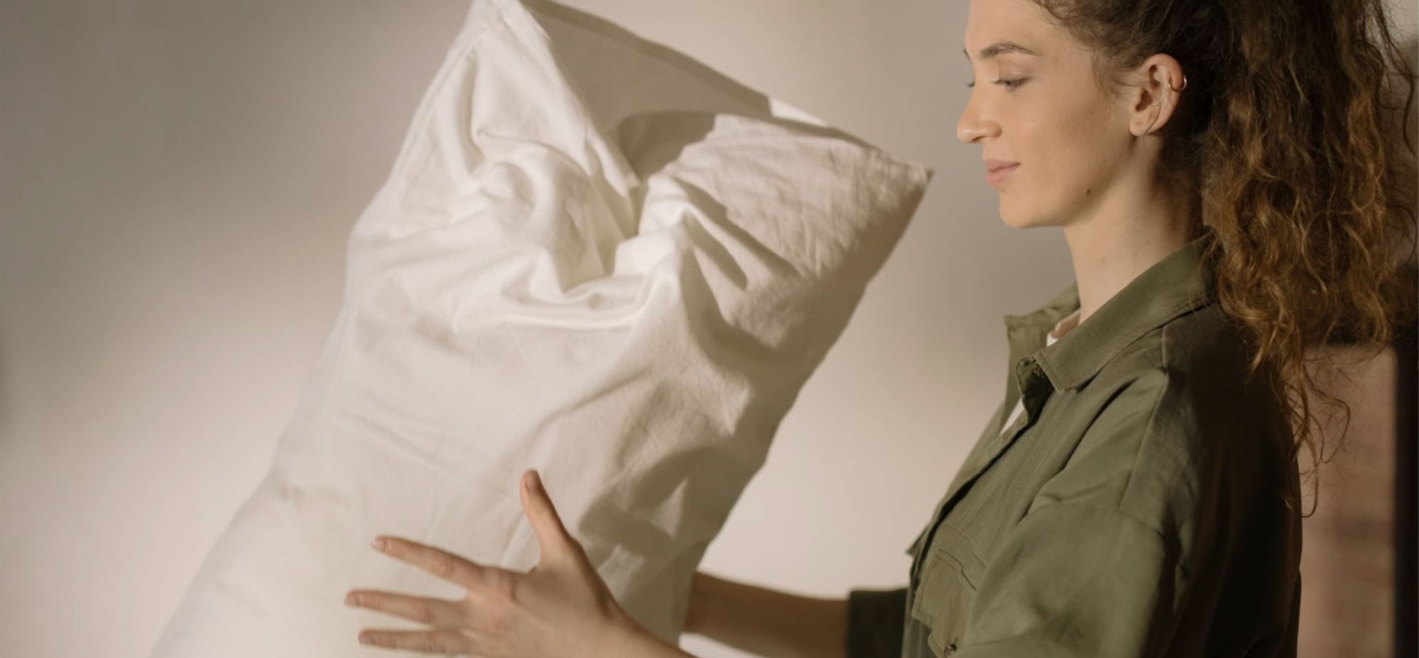 Woman changing the bedding and fluffing up a pillow for a clean home