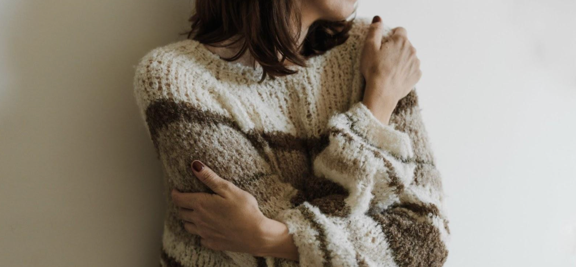 Woman hugging herself in a cosy winter jumper.