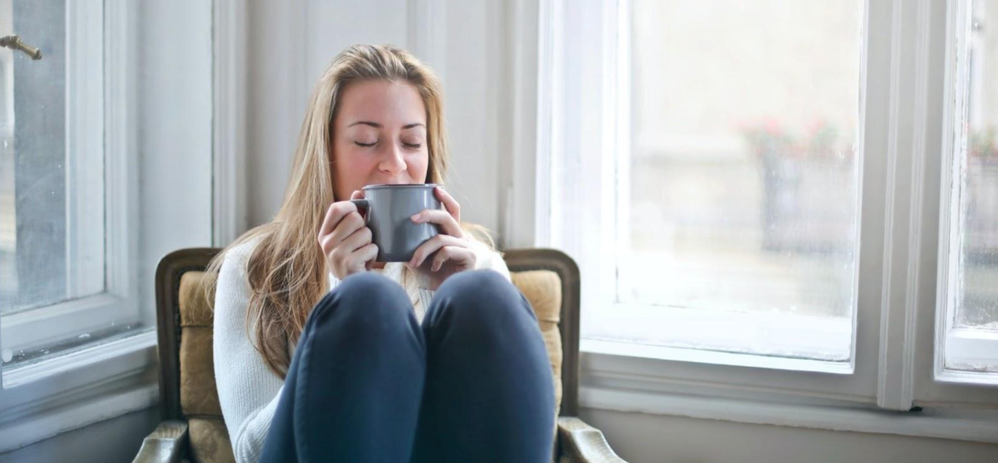Woman curled up, drinking a cup of coffee for her mental health in winter.