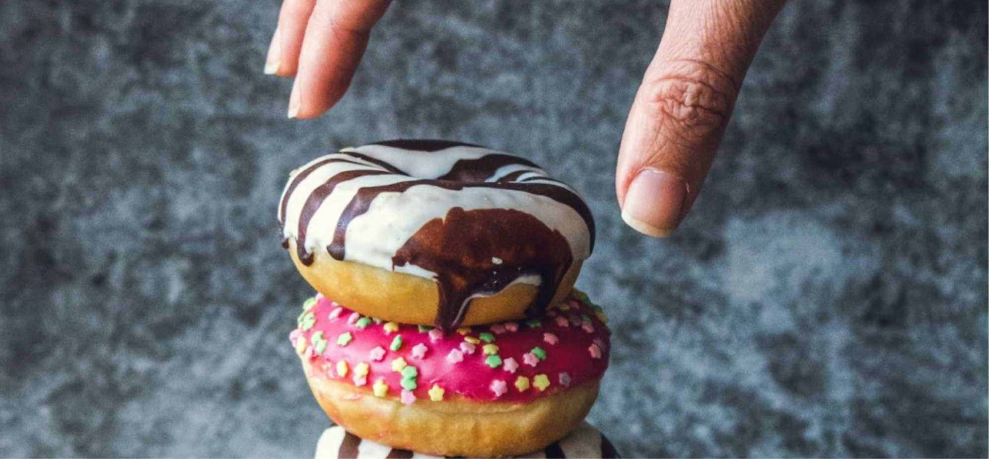 Person’s hand reaching for a pile of sugary, iced doughnuts