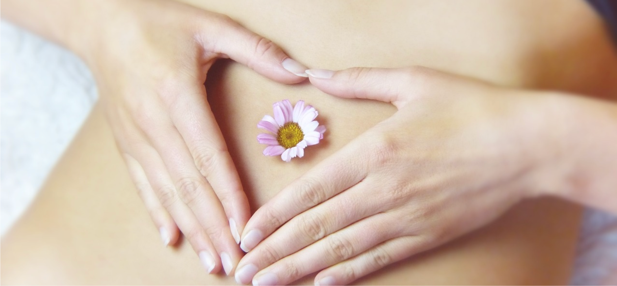 Woman with her hands on her stomach, making a heart shape with a small flower in the centre