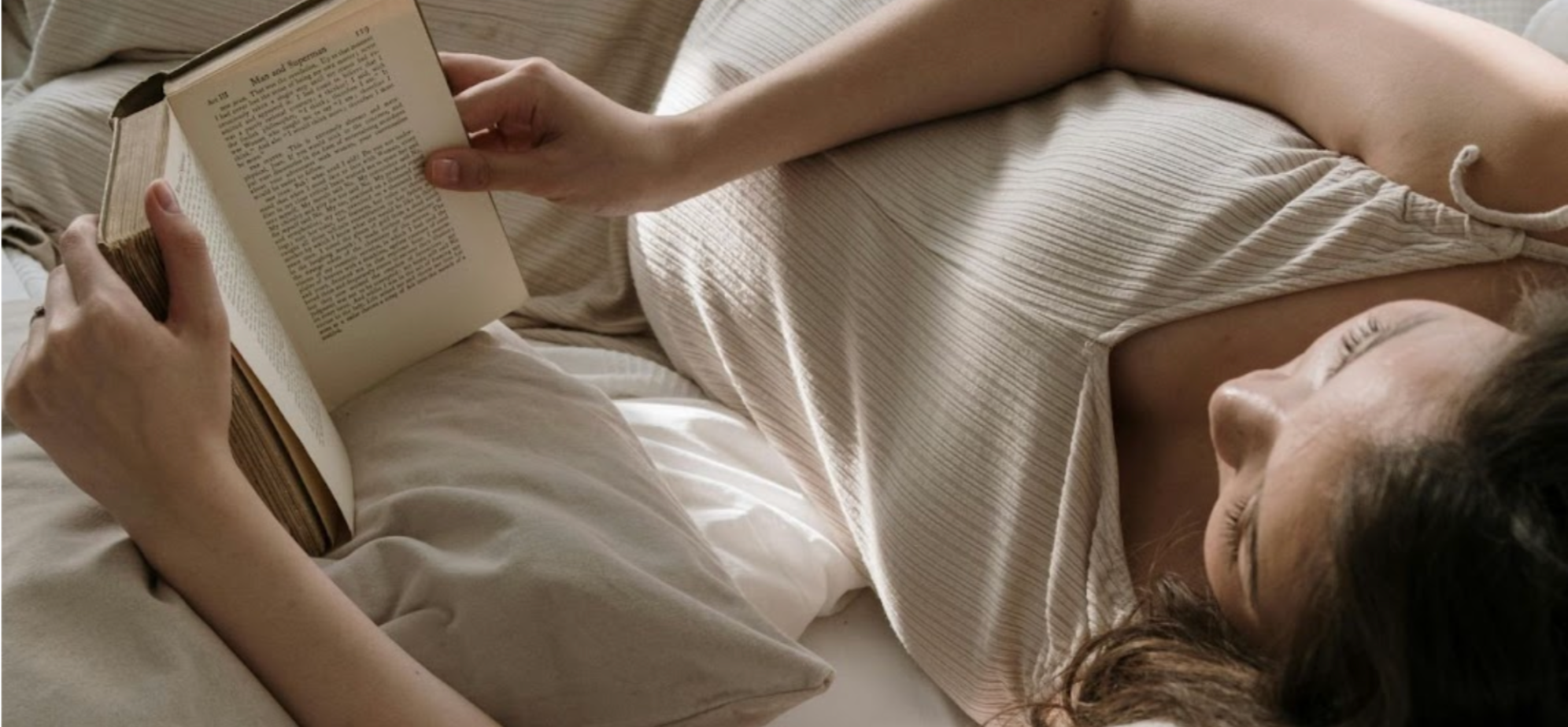 Woman reading a book in a white bed