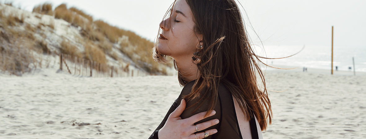 Collagen: Woman hugging herself, with closed eyes, on a beach.