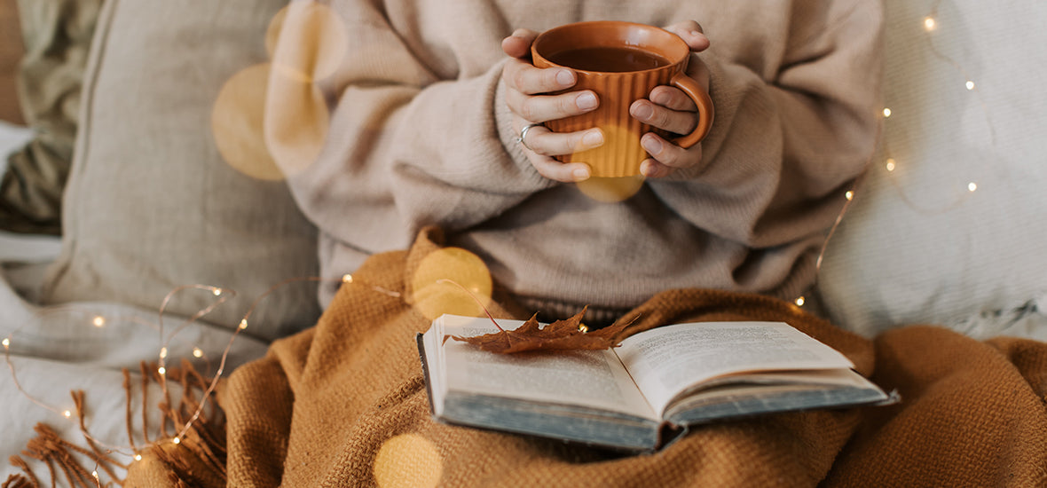 Cosy blanket and book with cradling hot drink to stay healthy in autumn.