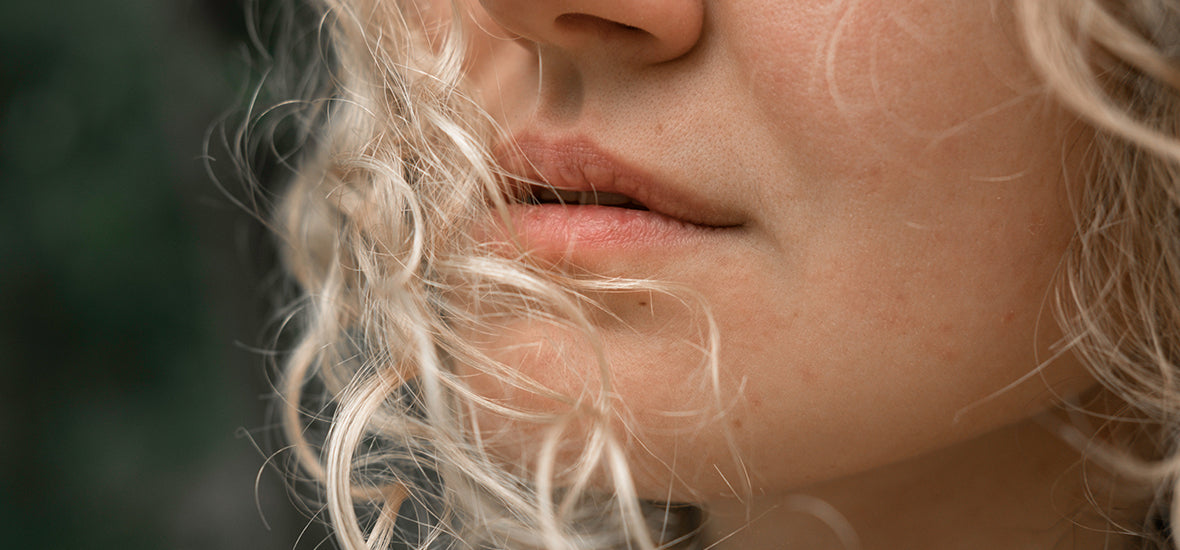 Close-up of woman’s lips with her curly white-blonde hair blowing in front.