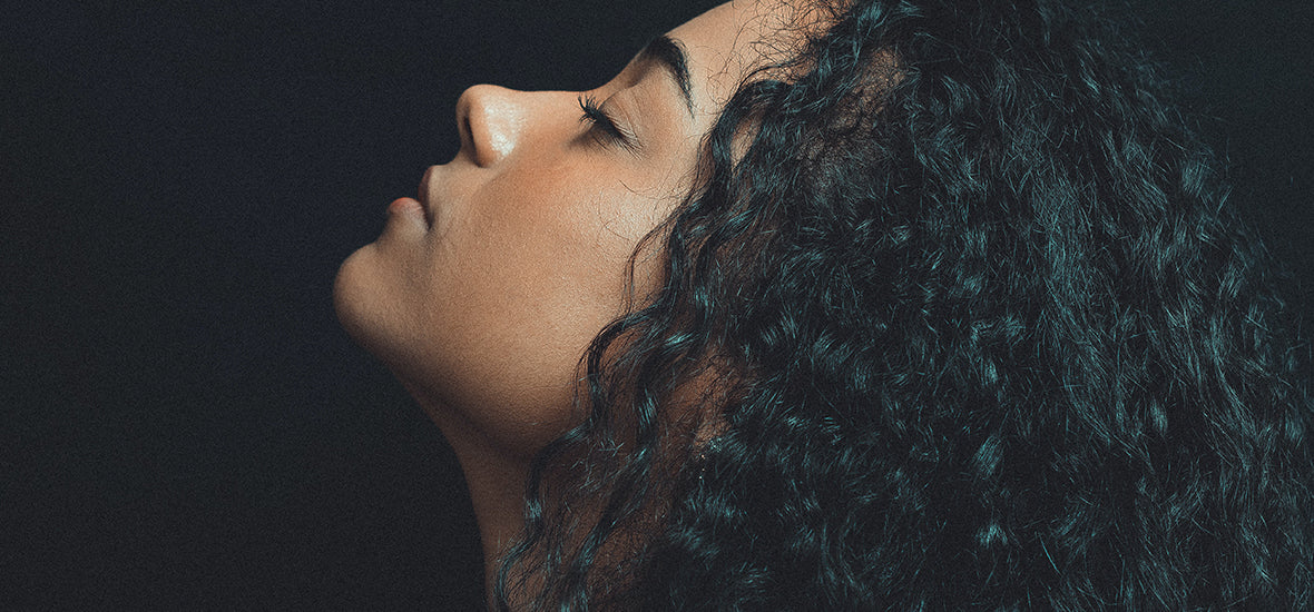 Close-up of black woman’s face, with her eyes closed and curly black hair, healthy from collagen for hair growth.