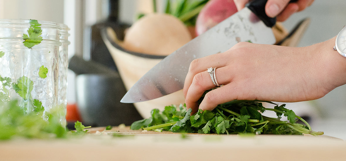 Woman’s hands, wearing a ring and chopping coriander with a large knife on her kitchen counter for her evening routine for sleep.