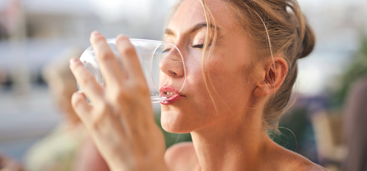 Close-up of woman with closed eyes, drinking water from a glass to hydrate her skin.