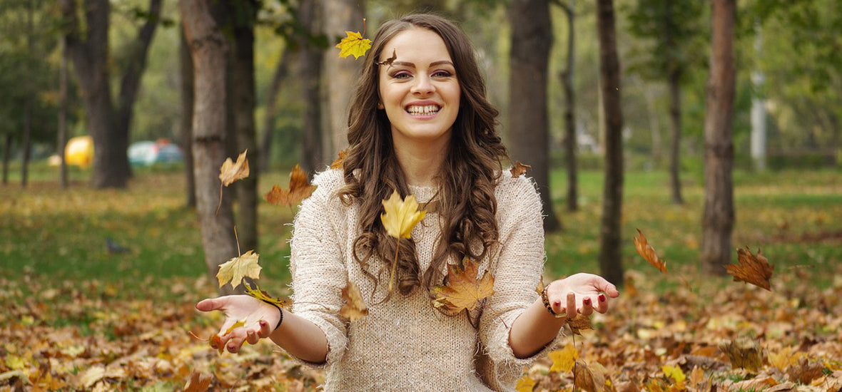 A smiling woman sat cross-legged on autumn leaves.