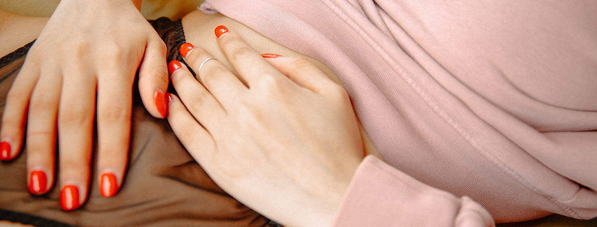 Collagen for gut health: woman in pink top and black pants, resting hands over the lower abdomen