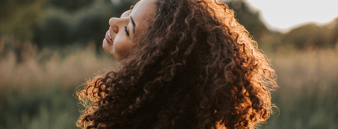 Collagen: Happy woman with brown curly hair in a field.