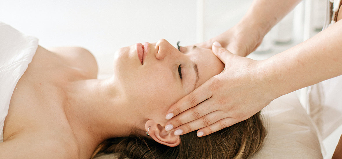 Woman with her eyes closed, lying down and getting a head massage to increase blood flow for hair growth.