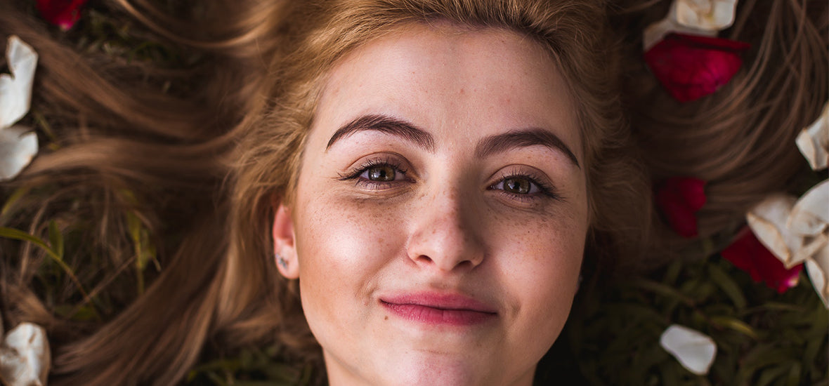 Close-up of woman’s smiling face, lying on the grass with her hair spread out and soft skin from using ginseng for skin.