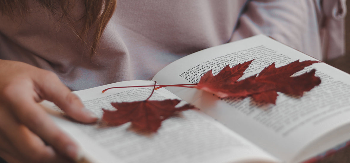 Woman holding a book with red autumn leaves.
