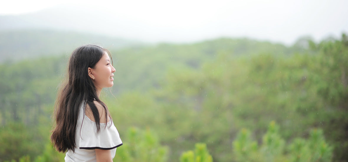 Asian woman with long brown hair looking out over a forest and smiling.