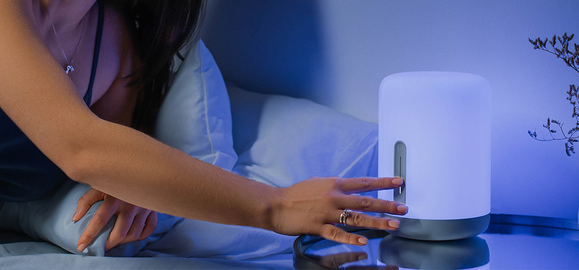 Woman leaning across to switch off her bedside lamp and diffuser as part of her evening routine for sleep.
