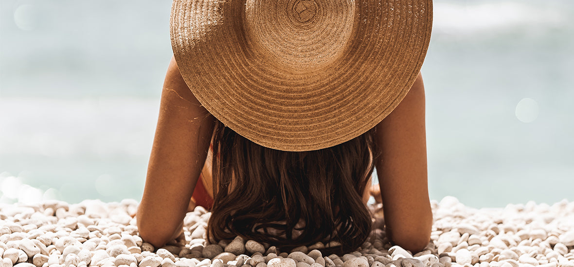 Boost collagen: Woman lying on the stone beach wearing a sun hat.