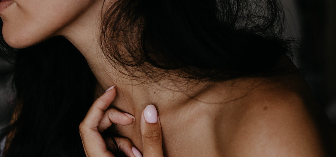 Close-up of brown woman’s bare shoulder with long dark hair.