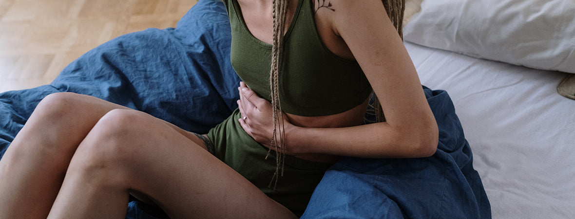 Collagen for gut health: Woman with dreadlocks in green yoga set holding stomach in pain.