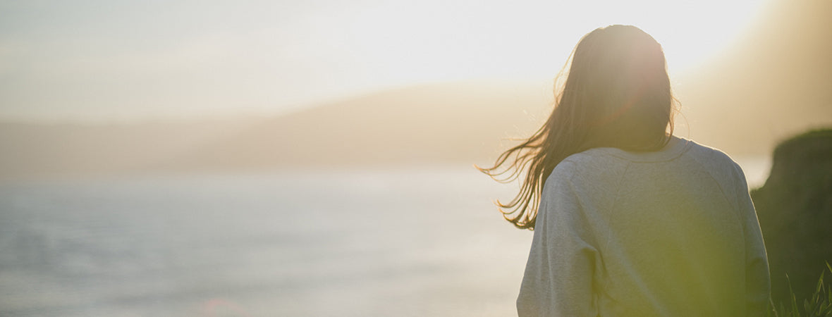 Person sitting by the coastline, watching the sunset.