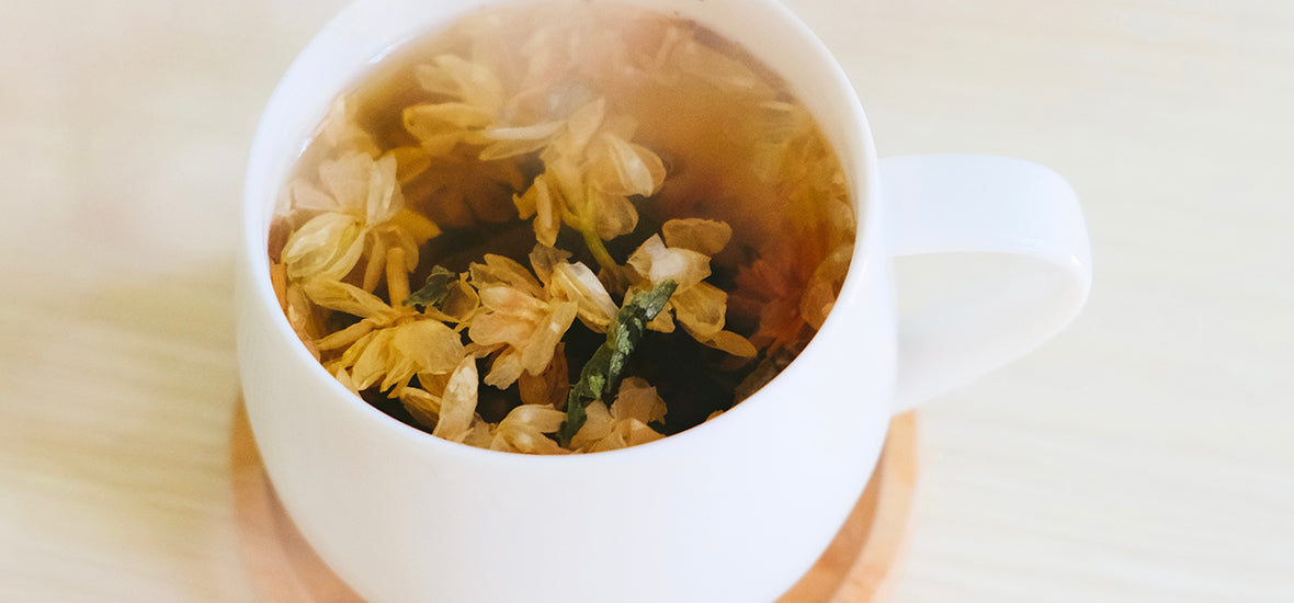 A white cup of herbal tea with pale yellow flowers as an evening routine for sleep.