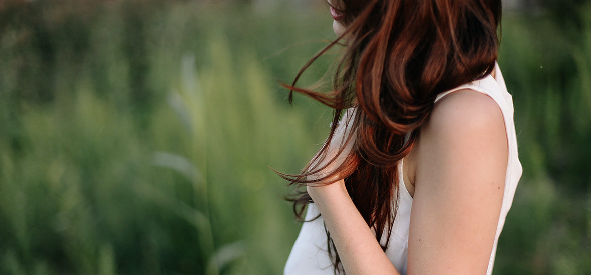 Close-up of a woman with red hair with her hand on her chest.