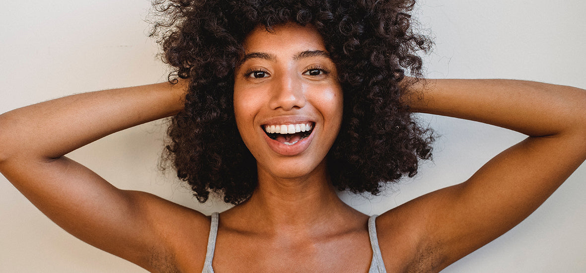 Black woman with hands on her curly hair and smiling from using VeCollal® collagen.