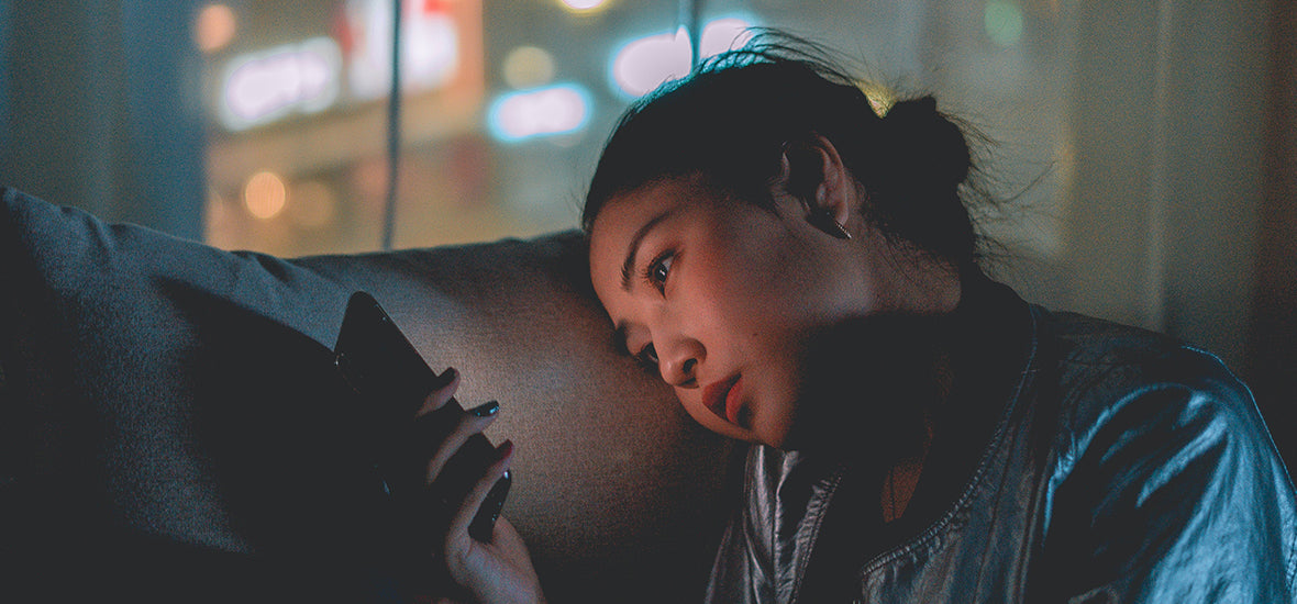 Asian woman leaning her head on the sofa in the dark, on her phone, and procrastinating on sleep.