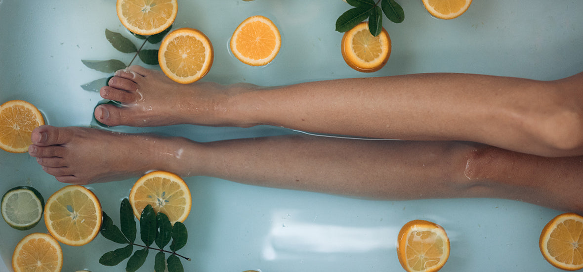 White woman’s long legs in the bath with orange, lemon, and lime slices instead of procrastinating her bedtime.