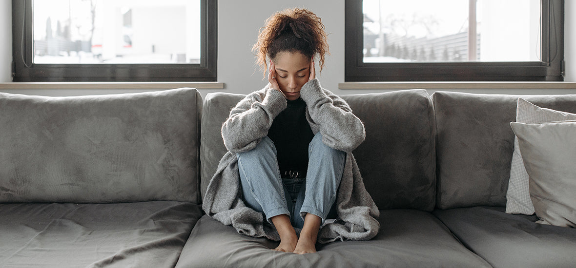 Woman on a grey sofa with a headache because of stress.