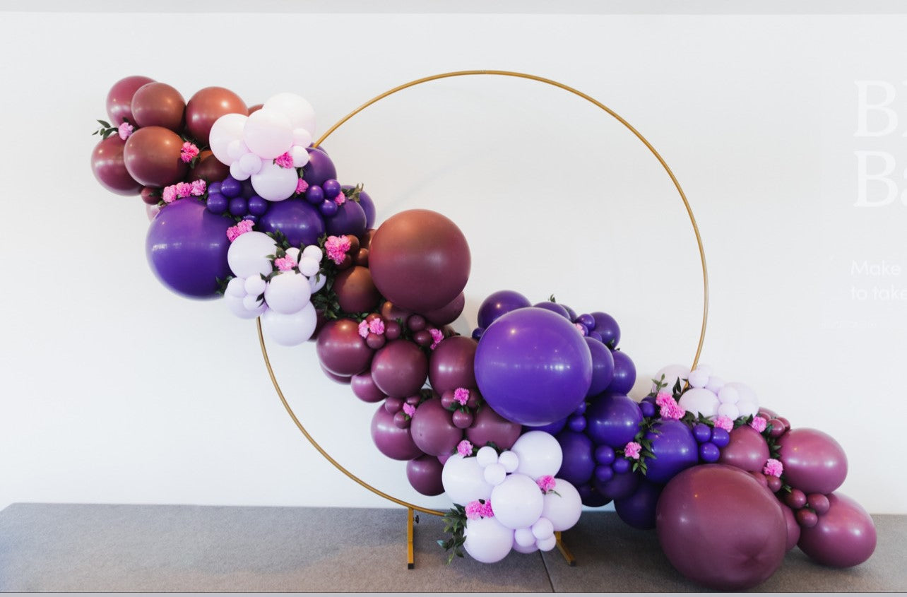 purple and pink balloon garland on angle across a gold hoop. 